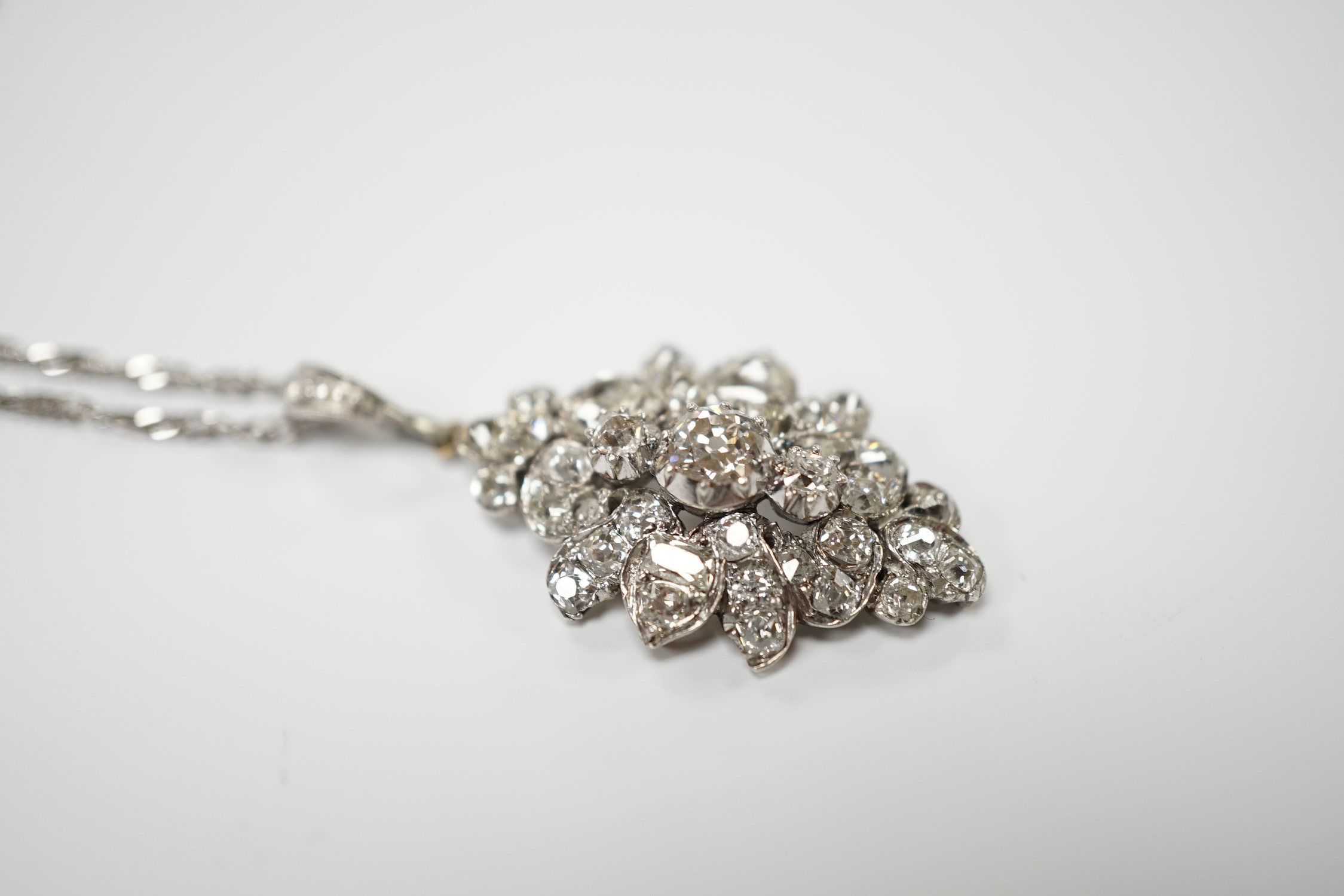 A white metal and diamond cluster set oval pendant, 27mm, on 9kt white metal chain, gross weight 5.8 grams.